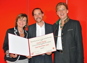 Kulturlandesrätin Sabina Kasslatter Mur (re.) und ihre Tiroler Amtskollegin Beate Palfrader gratulieren dem Künstler Markus Bacher zum Paul-Flora-Preis.